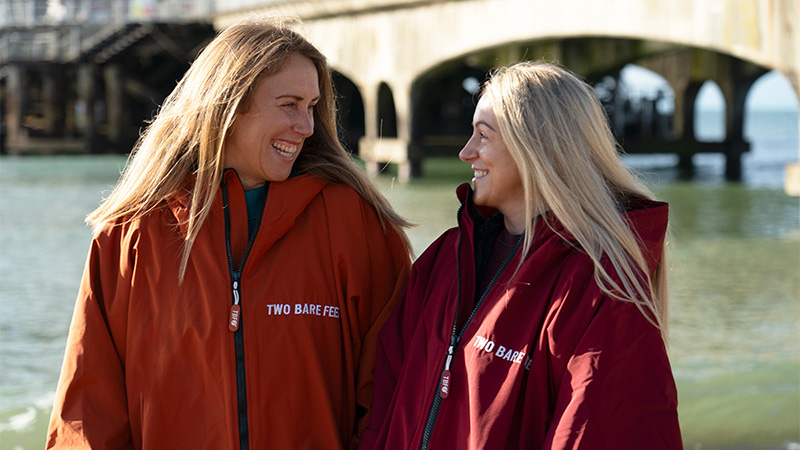 Two people wearing Two Bare Feet changing robes by the sea