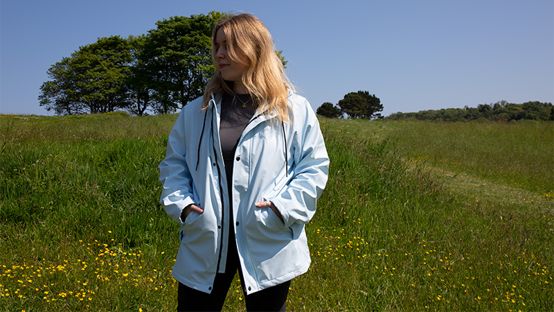 Woman wearing a light blue Two Bare Feet waterproof jacket in a field