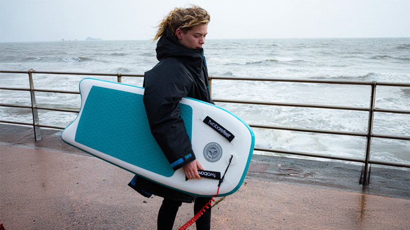 Person holding a Two Bare Feet inflatable bodyboard by the sea