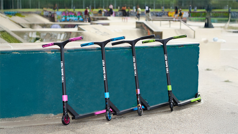 Row of colourful Two Bare Feet stunt scooters at a skate park