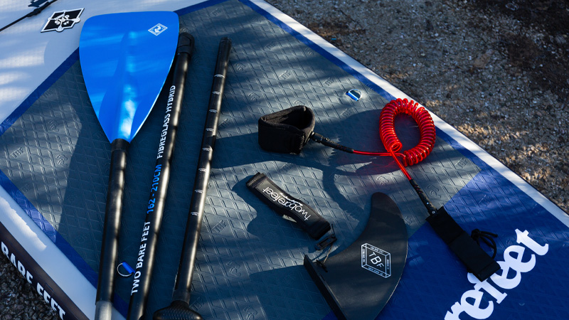 Two Bare Feet SUP accessories including paddle, leash, and fin laid out on a paddleboard
