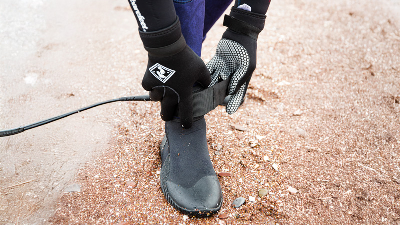 Close-up of person fastening neoprene wetsuit boots and gloves on the beach