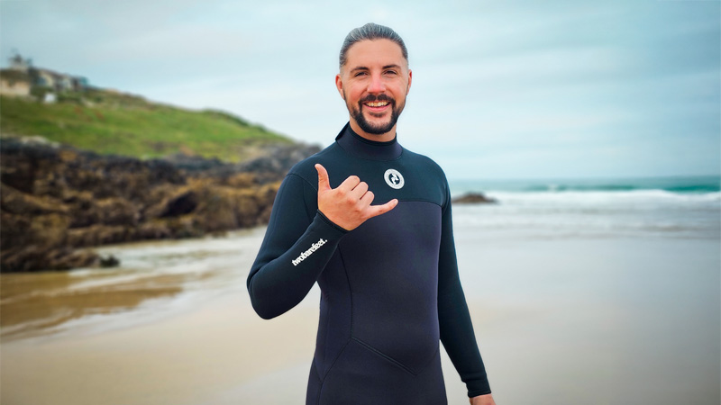 Man wearing a black Two Bare Feet wetsuit smiling on the beach