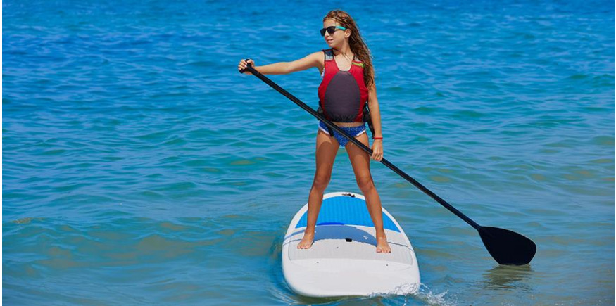 Child standing on inflatable paddle board with SUP paddle in hands
