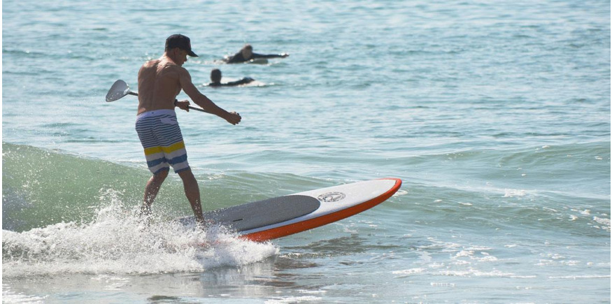 Paddleboarder riding surf on inflatable SUP with paddle in hand