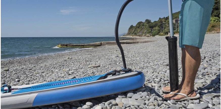 Paddler inflating an iSUP on a beach using SUP pump attached to board valve