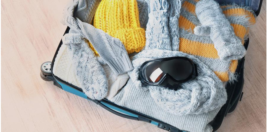 Warm, wool snowboard clothing and snow goggles packed in a suitcase