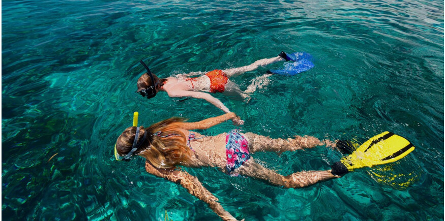 3 children snorkelling in clear blue water in the ocean