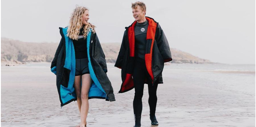 Male and female paddleboarders wearing wetsuit layers on beach