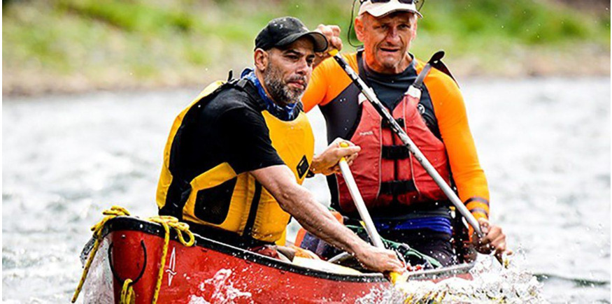two men in a canoe wearing buoyancy aids paddling down river 