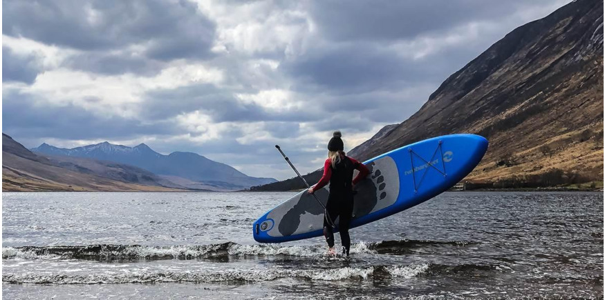 girl carrying an inflatable sup into a cold scottish loch