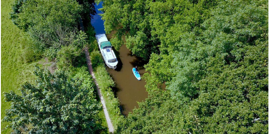 paddleboarding down an overgrown section of river shot from above by a drone