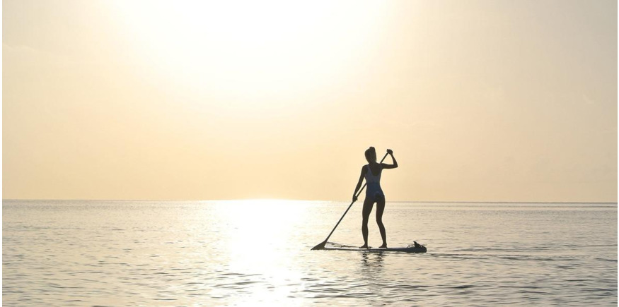 paddleboarder on glassy water during sunset