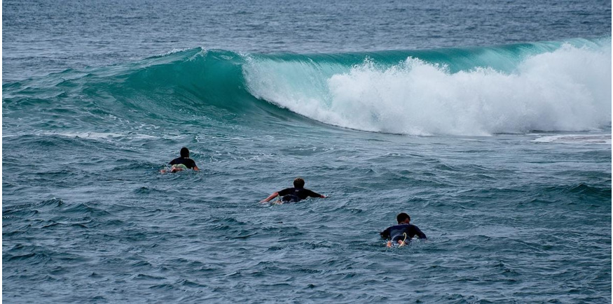 three surfers paddle out into the lineup towards a wave