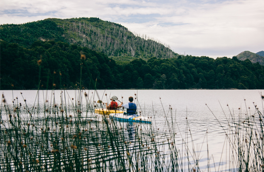 two kayakers paddling across a lake while wearing buoyancy aids
