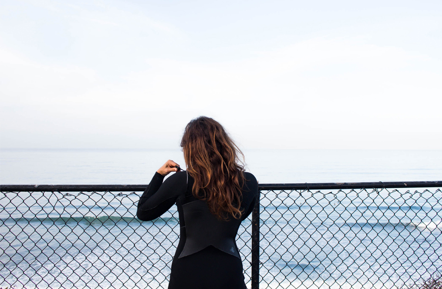 girl wearing a wetsuit looking out at the sea