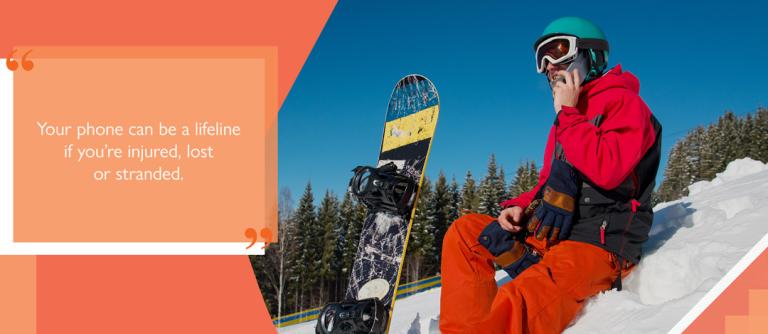 Man with snowboard, wearing helmet, snow goggles, ski jacket, snow pants and gloves, using mobile phone while sat on snow