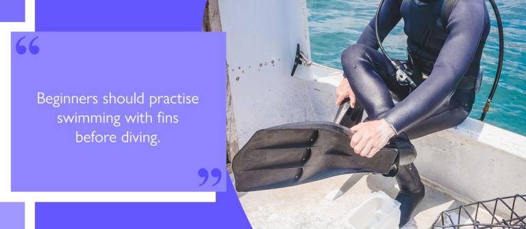 Diver sitting on boat's edge putting on fins prior to dive