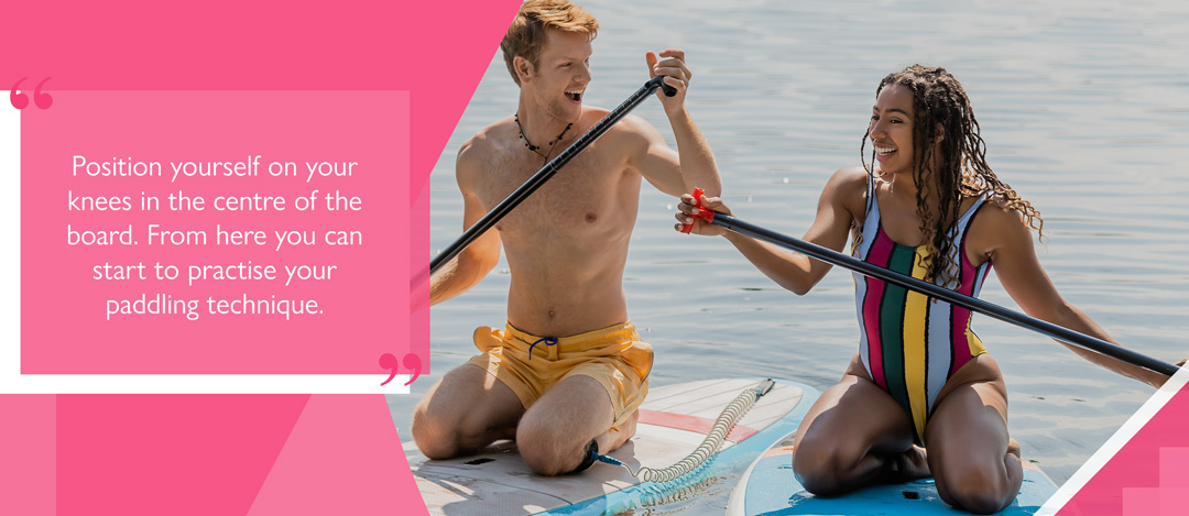 two people sit-down paddleboarding with text reading 'Position yourself on your knees in the centre of the board. From here you can start to practise your paddling technique'