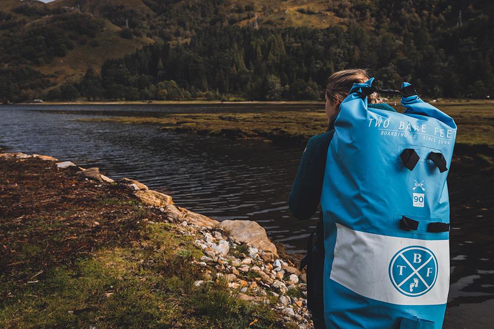 walking next to a lake carrying an inflatable paddleboard rucksack