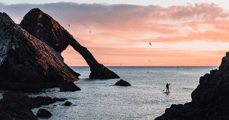 person paddleboarding between cliff faces at sunset